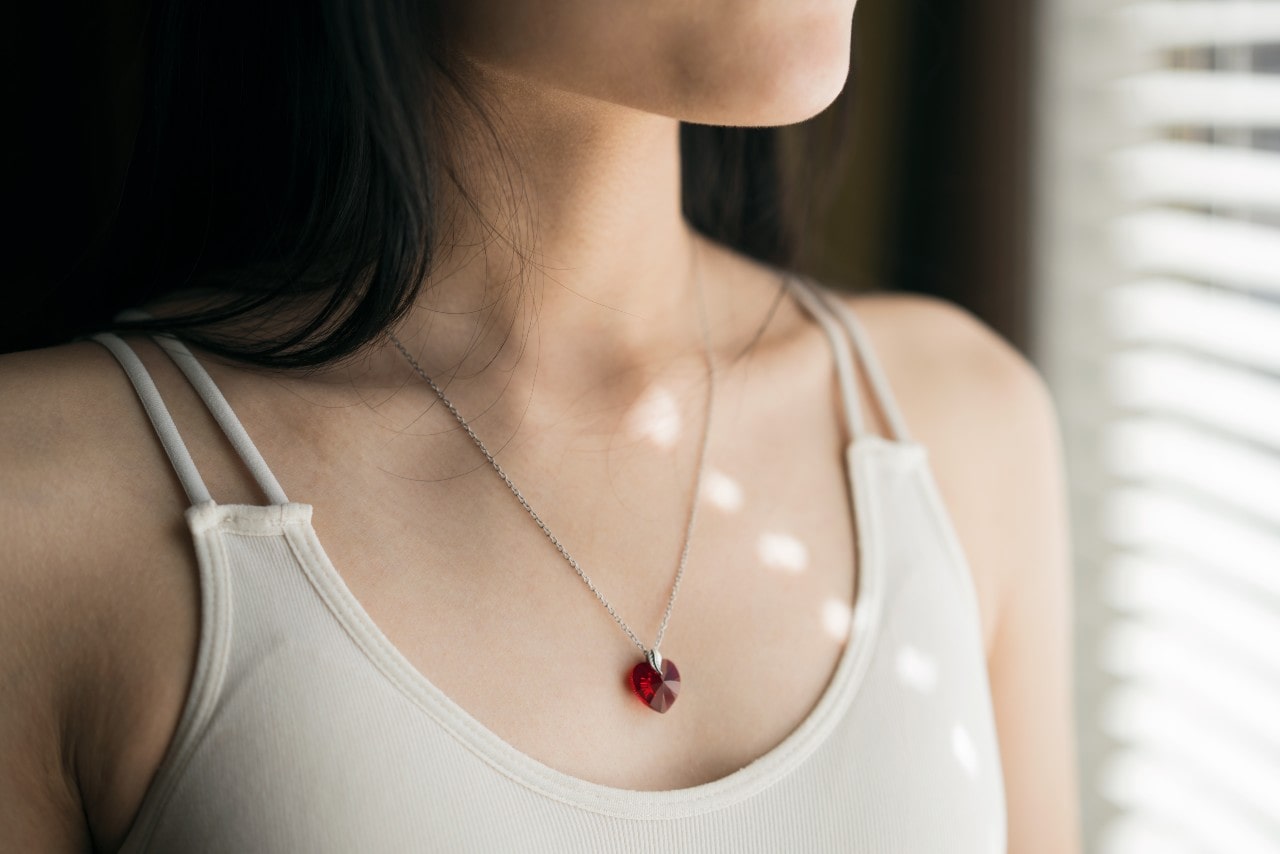 A close up of a woman&rsquo;s neck, showcasing a white gold chain pendant necklace with heart shaped ruby.