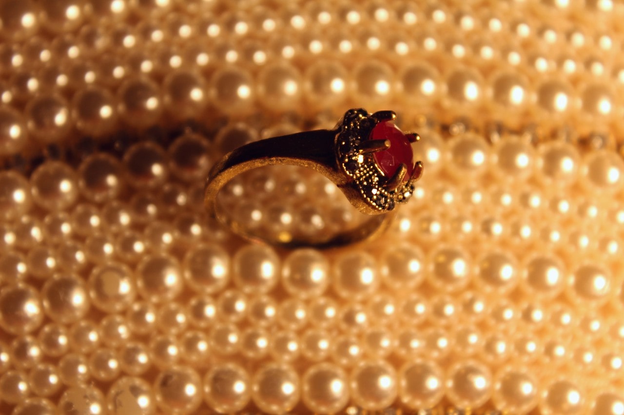 A close up of a vintage white gold ring with ruby on top of the pearls.