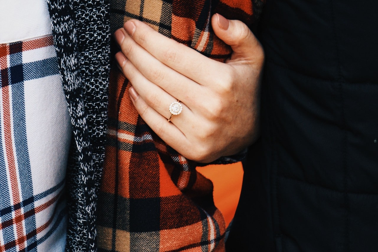 A woman’s hand wearing an engagement ring grabs her partner’s arm, wrapped in flannel.