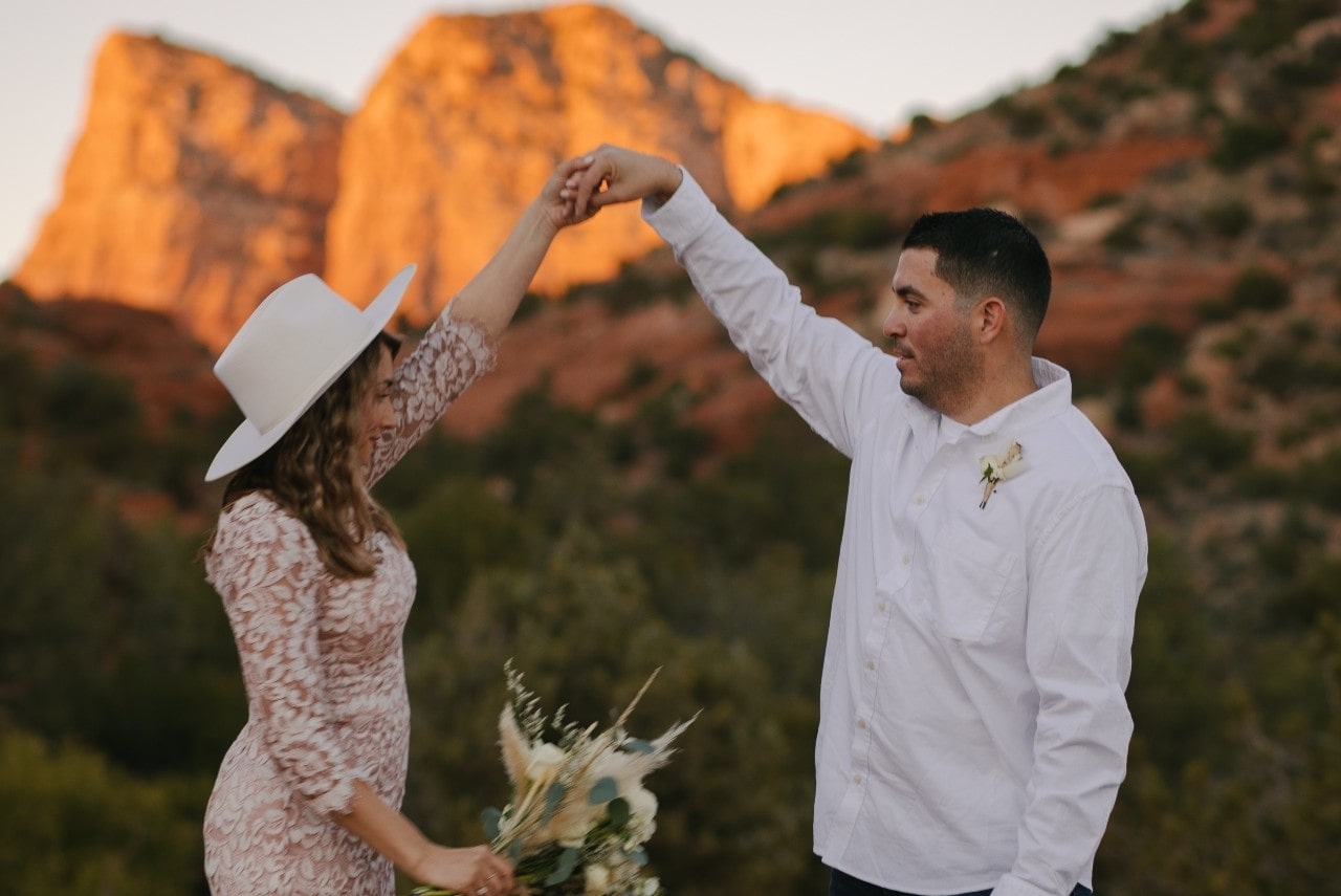 a happy couple holding hands and dancing beside some mountains