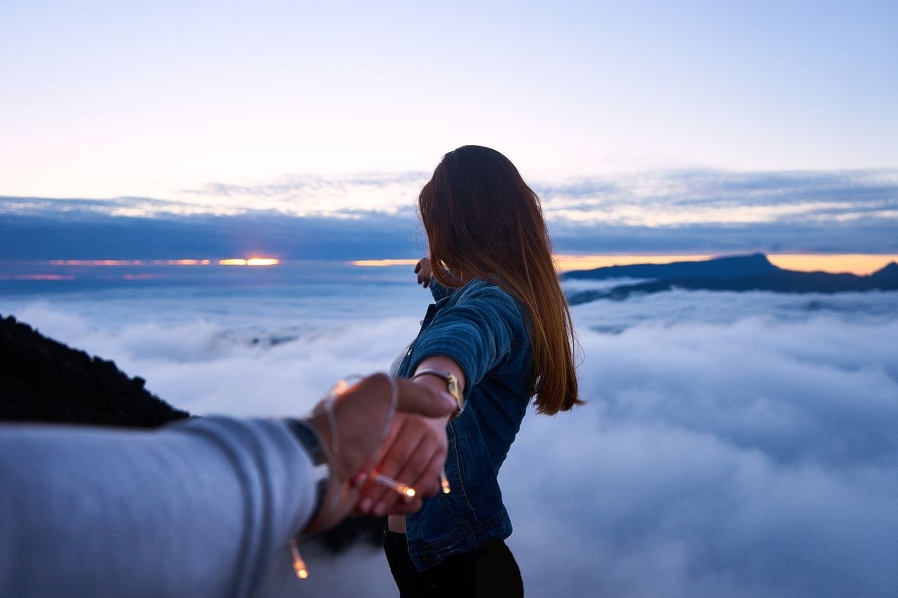man and woman holding hands from up high, looking out over the clouds