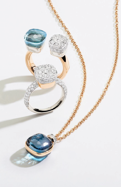 A yellow gold necklace with blue gemstone laid near the two ring one with diamonds and gemstones.