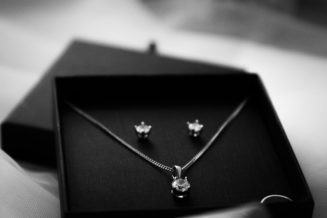 A black and white close-up of a matching jewelry set featuring diamond stud earrings and a diamond pendant necklace.