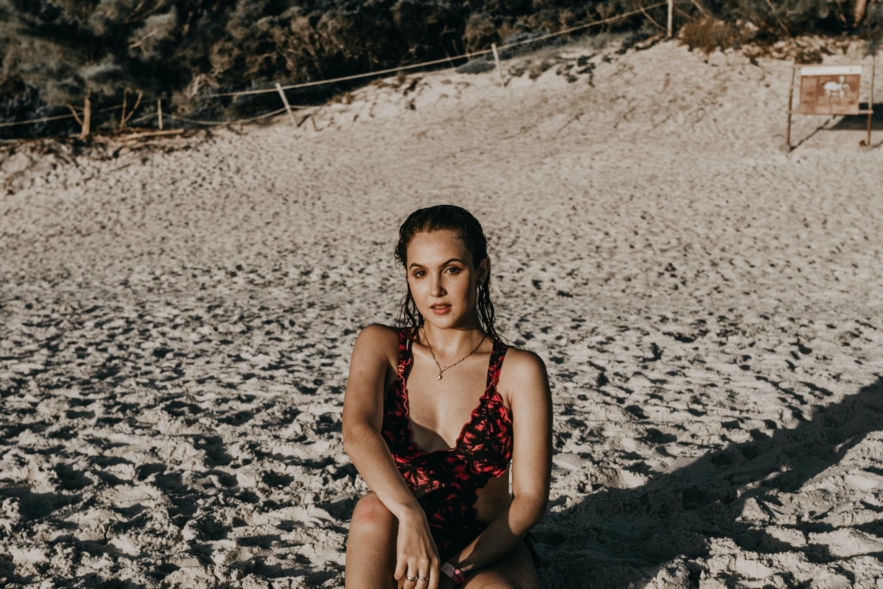 A young woman in a swimsuit sitting on the shore at the beach.