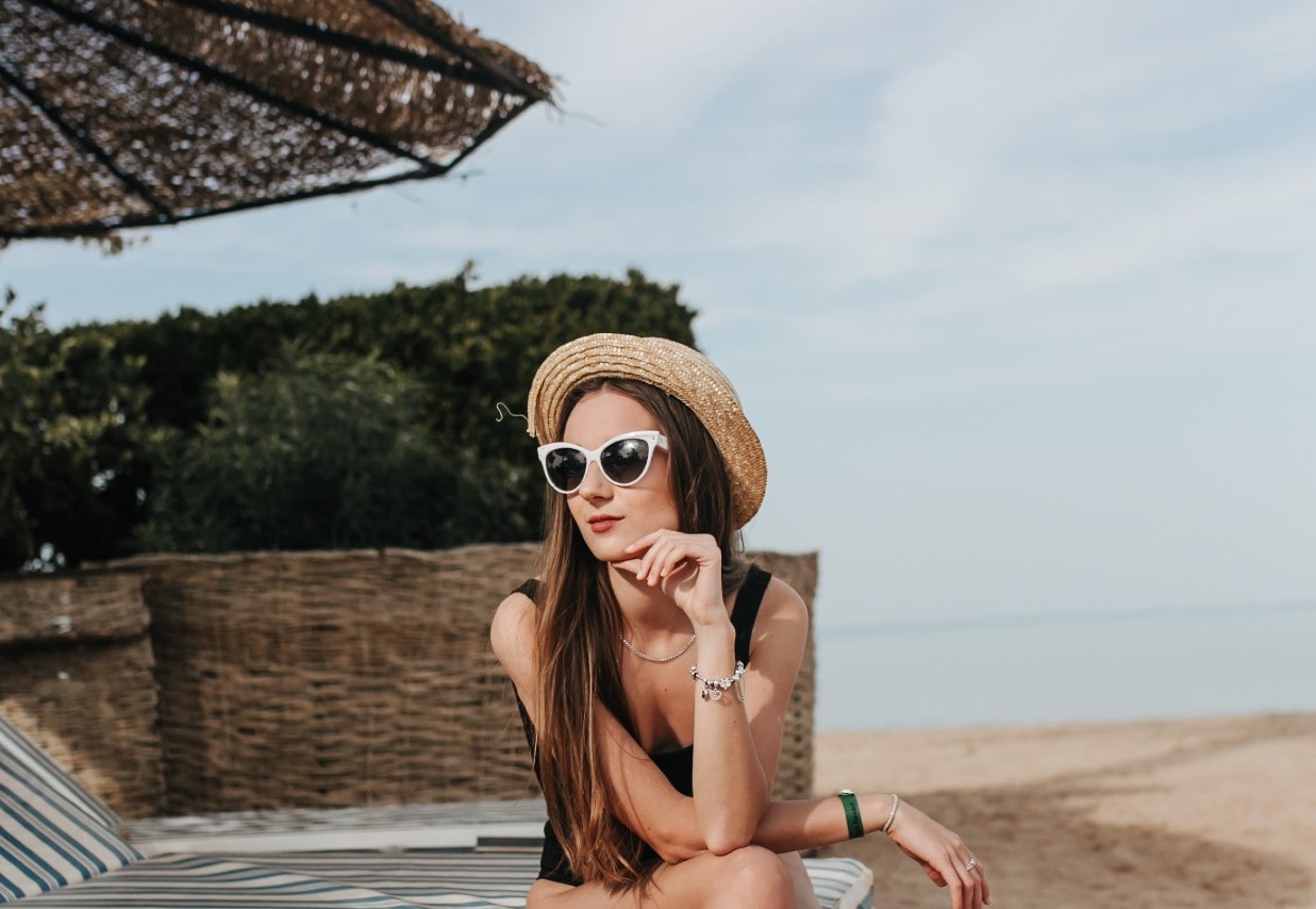 A wide-angle view of a stylish young woman relaxing at the beach.
