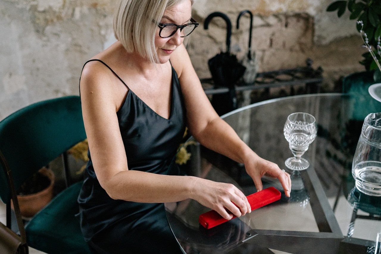 A woman sitting at a table about to open a red necklace box.