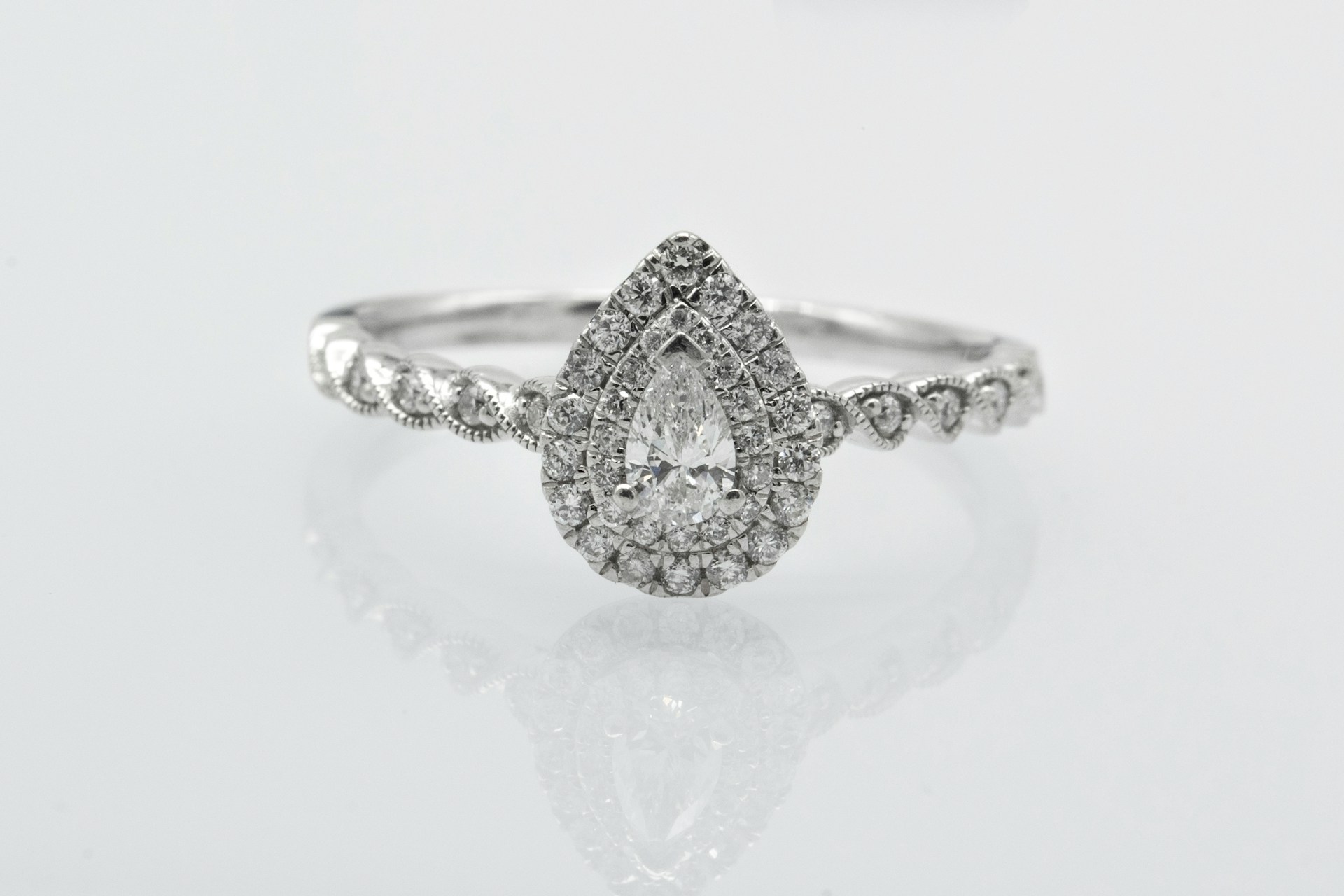 a pear shape engagement ring with a double halo, side stones, and milgrain detailing