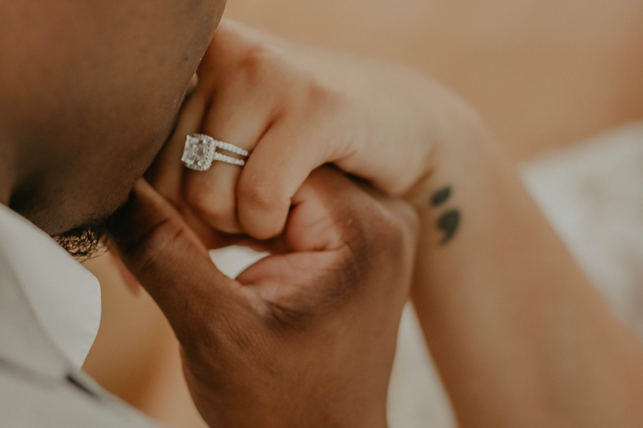 a man kissing a woman’s hand adorned with a halo engagement ring and diamond wedding band