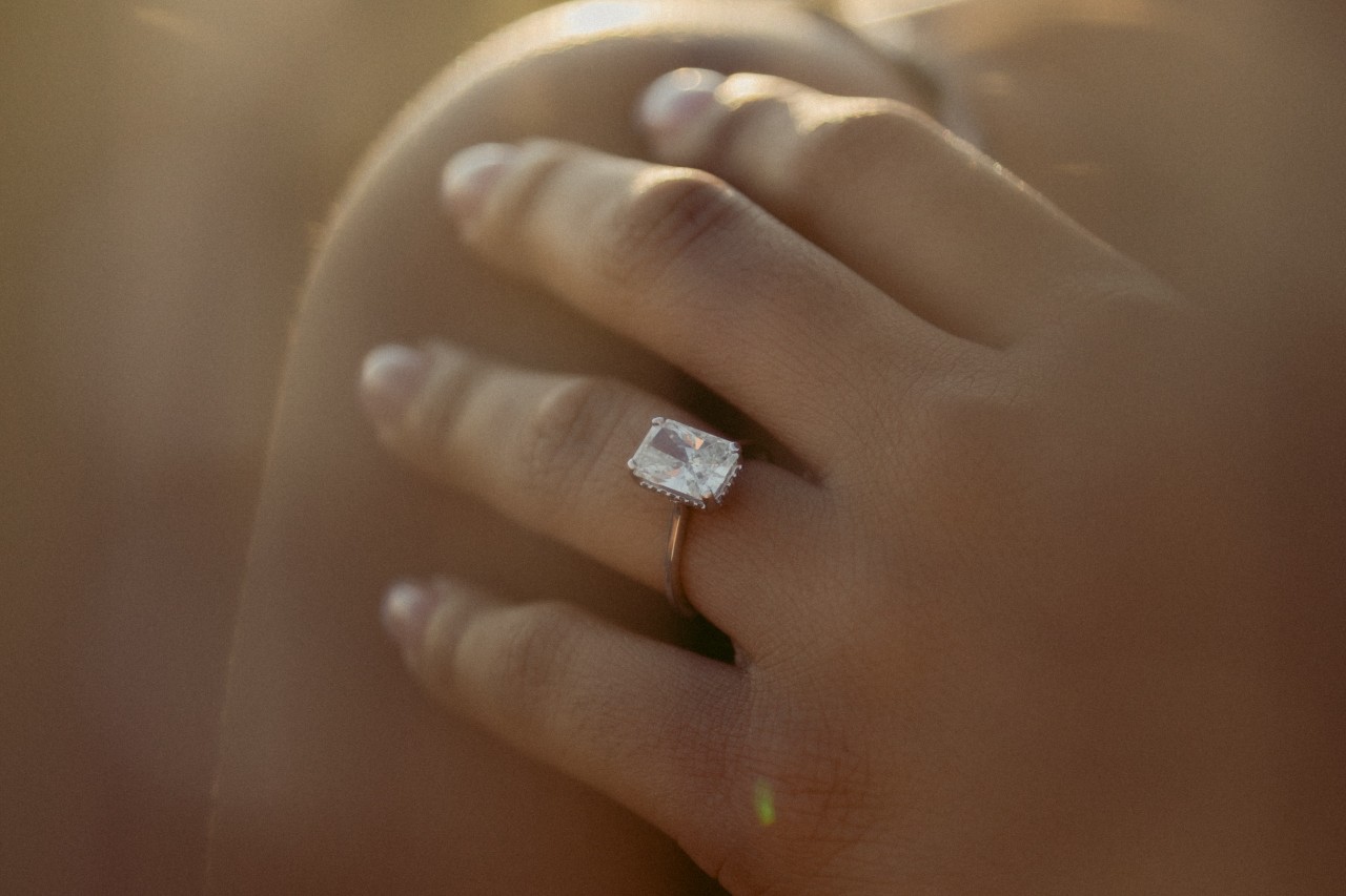 close up image of a woman’s hand on her shoulder, wearing a rose gold solitaire engagement ring