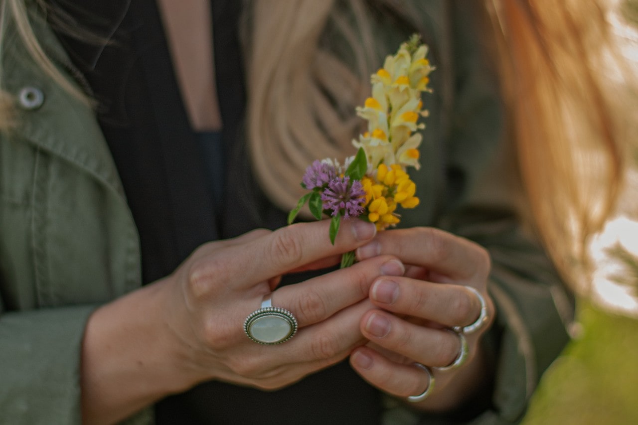 A woman holding a bouquet of tiny handpicked flowers, her large opal ring adorning her hand.