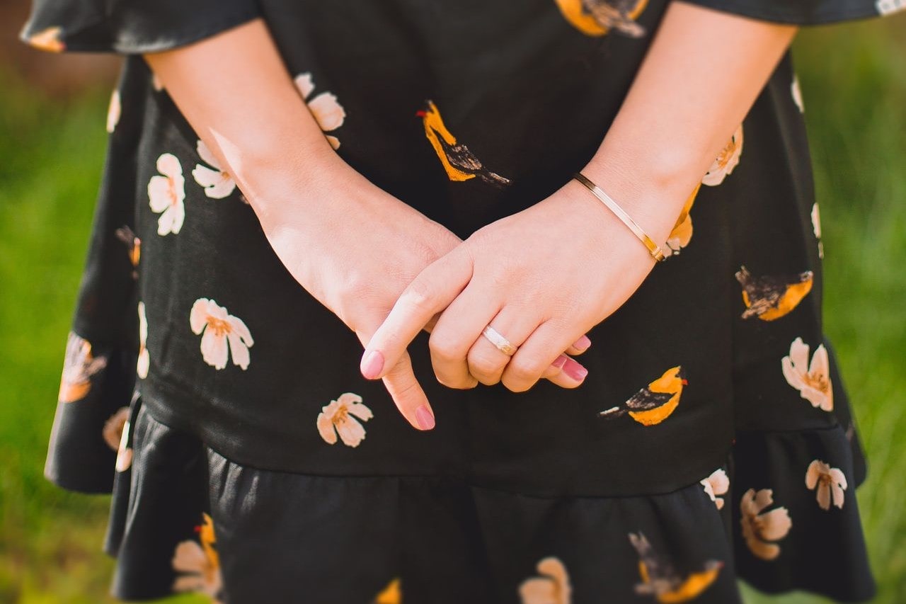 A woman holding her hands behind her back and showcasing her gold bracelet and matching gold ring.