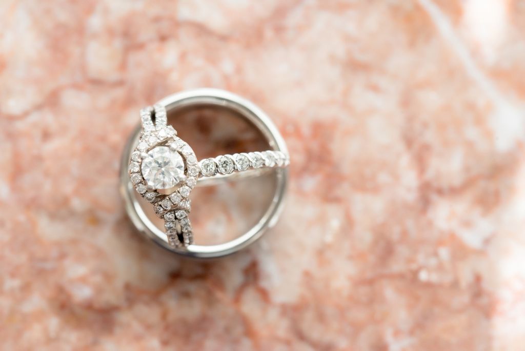 A diamond side stone engagement ring on top of the polished white gold wedding band on the marble surface