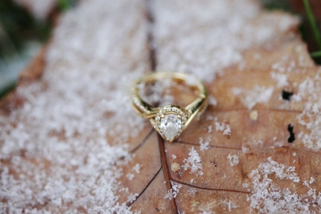 A yellow gold pear shaped diamond engagement ring on top of the leaf dusted with snow.