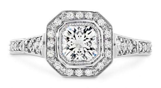 A bezel set cushion cut diamond with round diamonds bezel set around the center stone to create a halo and diamonds along the band.