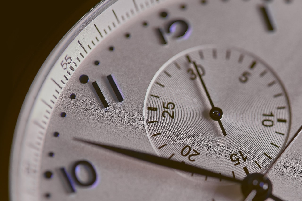 A close-up of a watch face featuring arab numerals and chronograph complication with black hands and detailing.