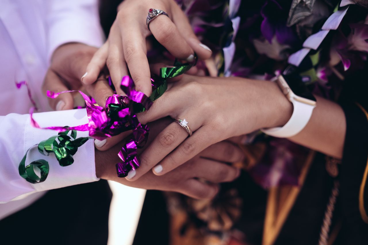 A bride wearing a princess cut ring ties a purple and green ribbon.