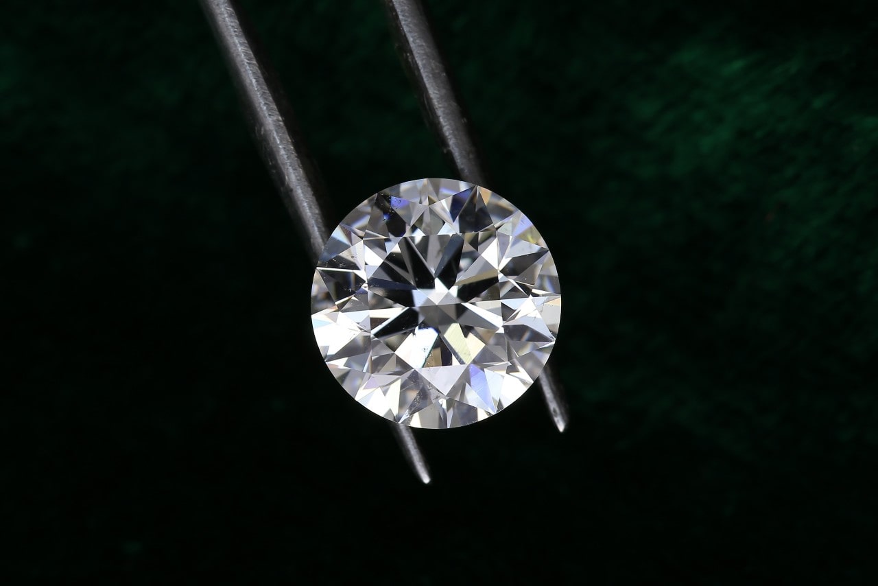 a pair of jeweler’s tweezers hold a round cut diamond in the light.