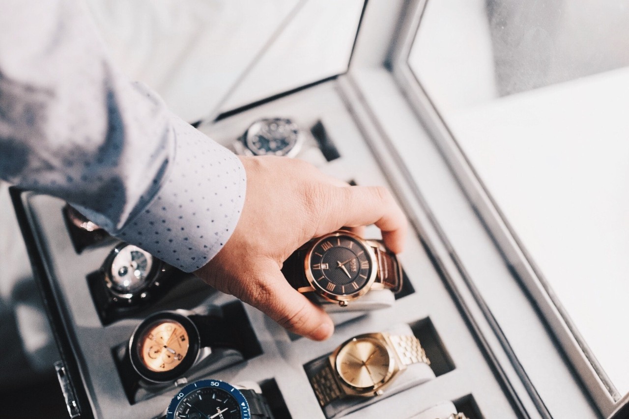 A man selects a watch from a large watch case.