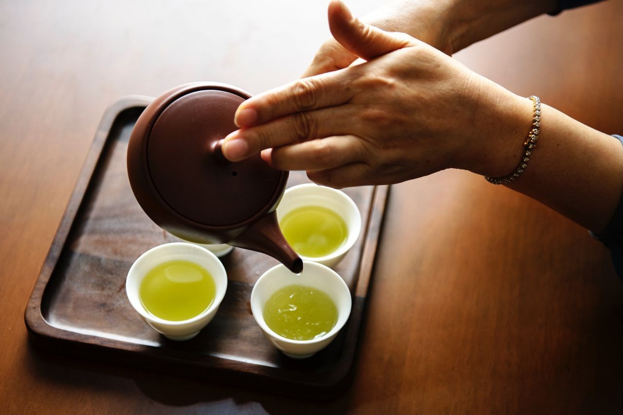 A woman wearing a tennis bracelet pours some green tea in small mugs.