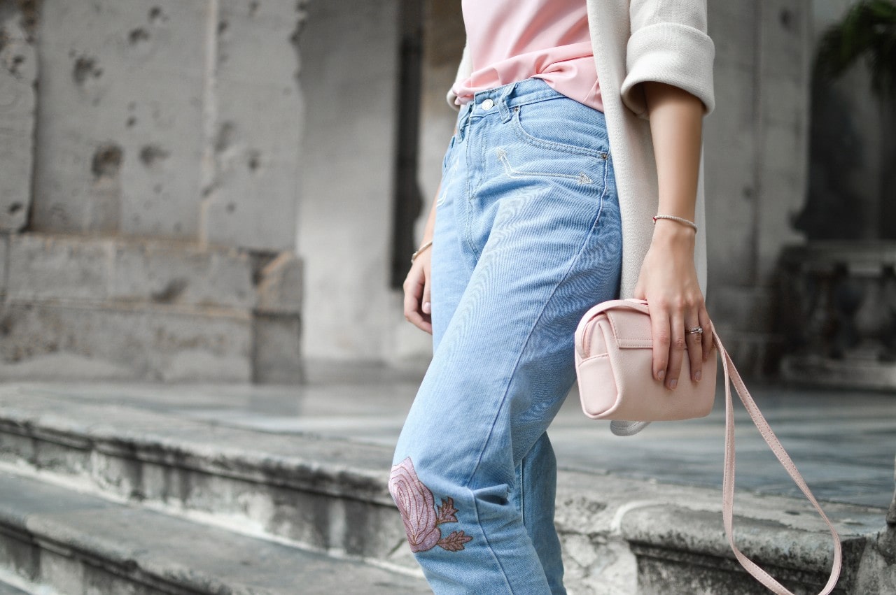 A woman wearing floral jeans, a pink purse, and a diamond bangle walks down stairs.