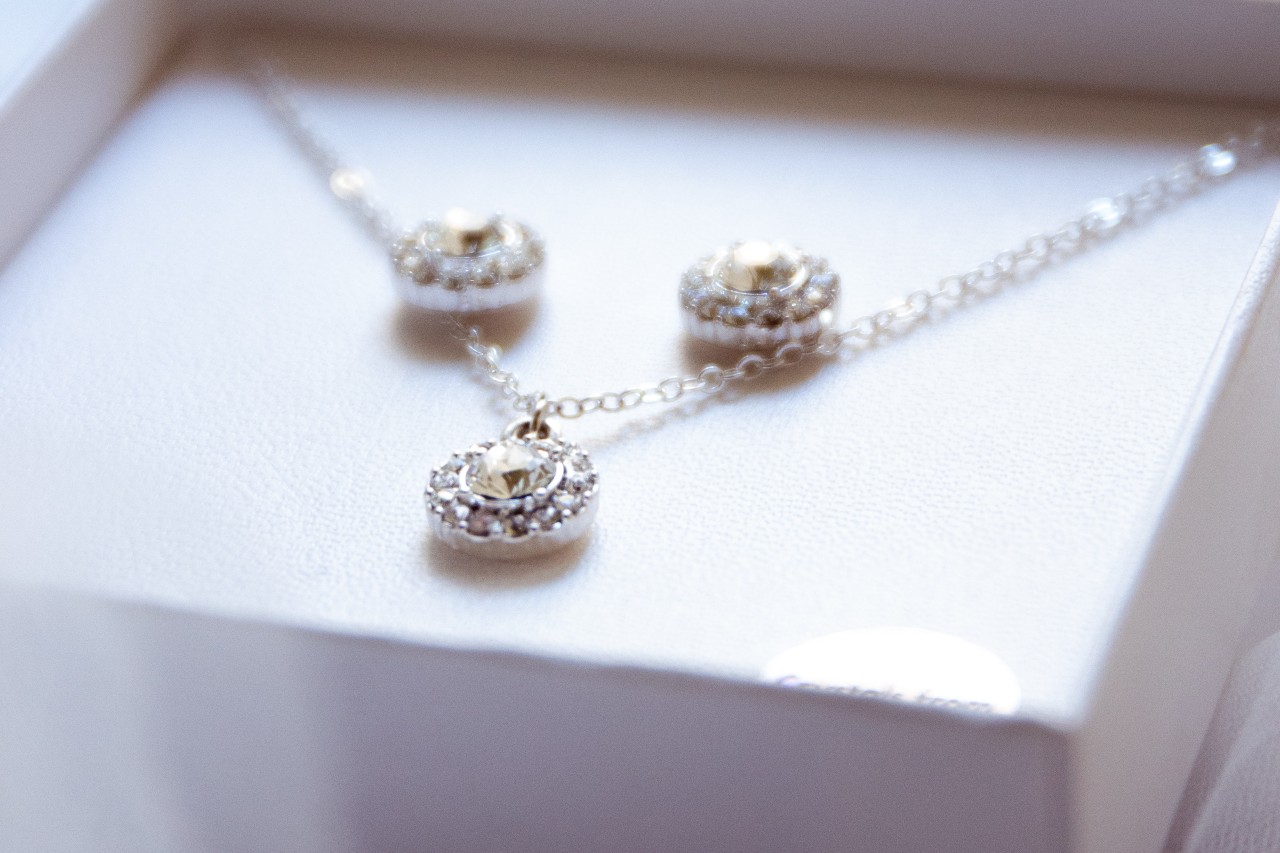 Elegant jewelry set in a white box, featuring a delicate necklace and matching earrings with circular pendants, each adorned with sparkling stones.
