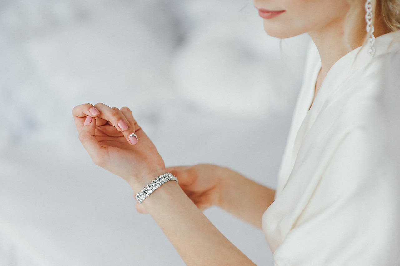 A woman in a white robe adjusts a sparkling diamond bracelet on her wrist.