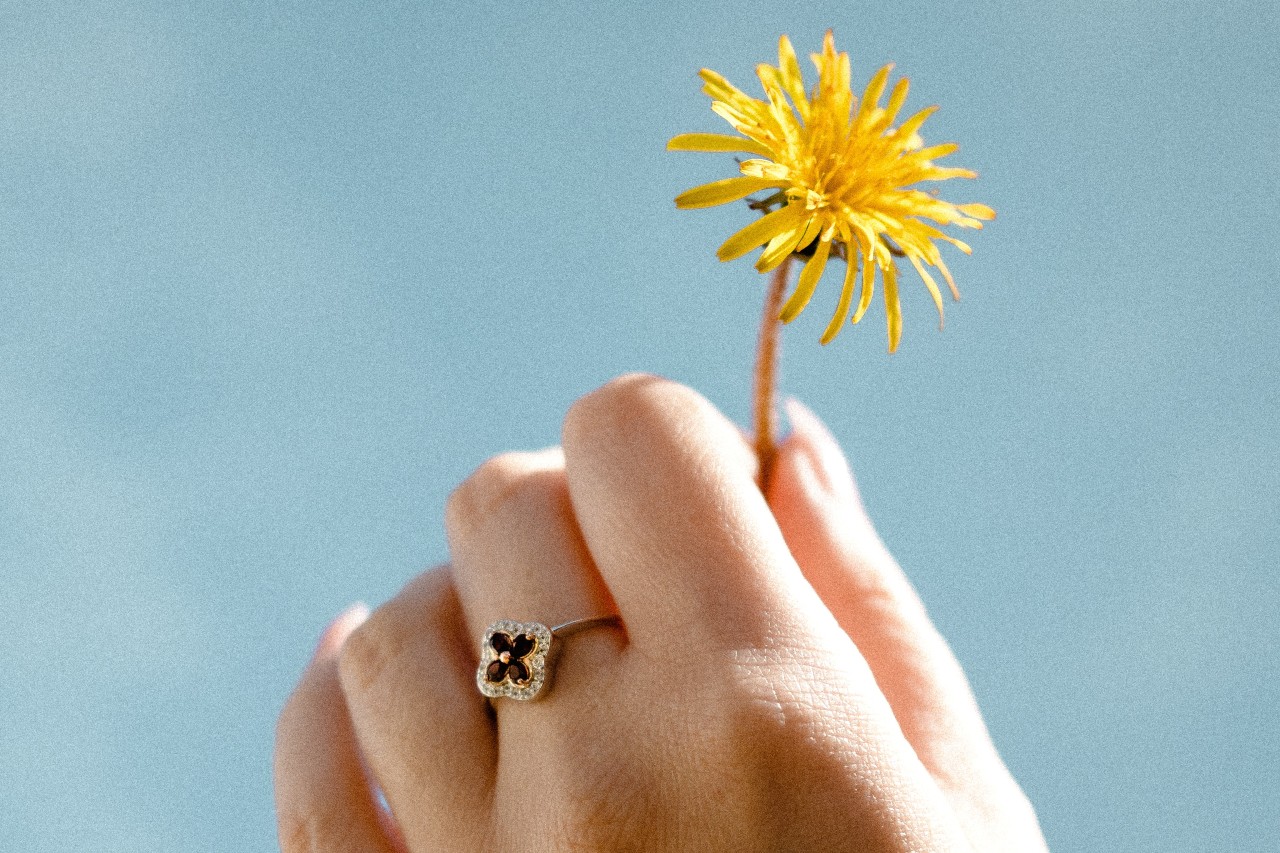 close up image of a hand holding up a dandelion and wearing a floral-inspired ring
