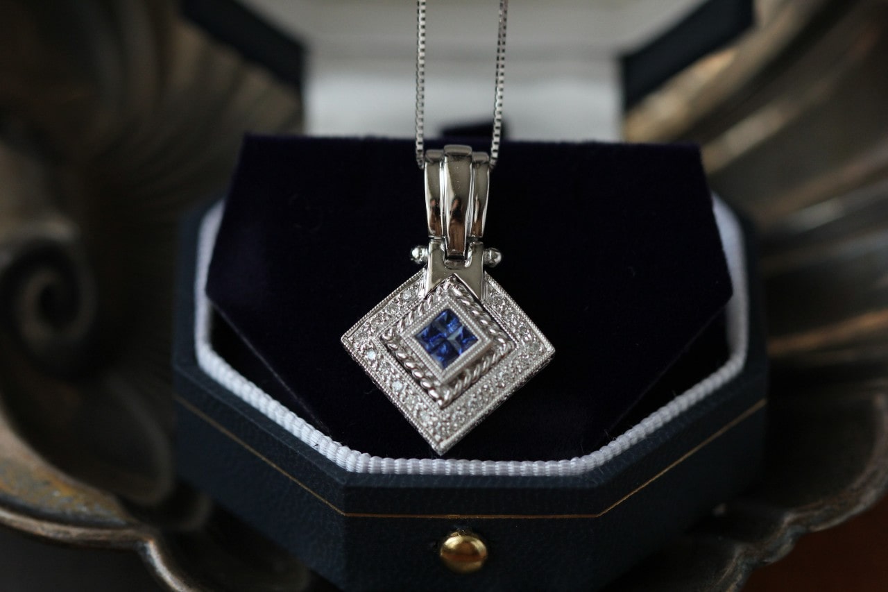 a white gold pendant necklace featuring sapphires at its center sitting in a jewelry box