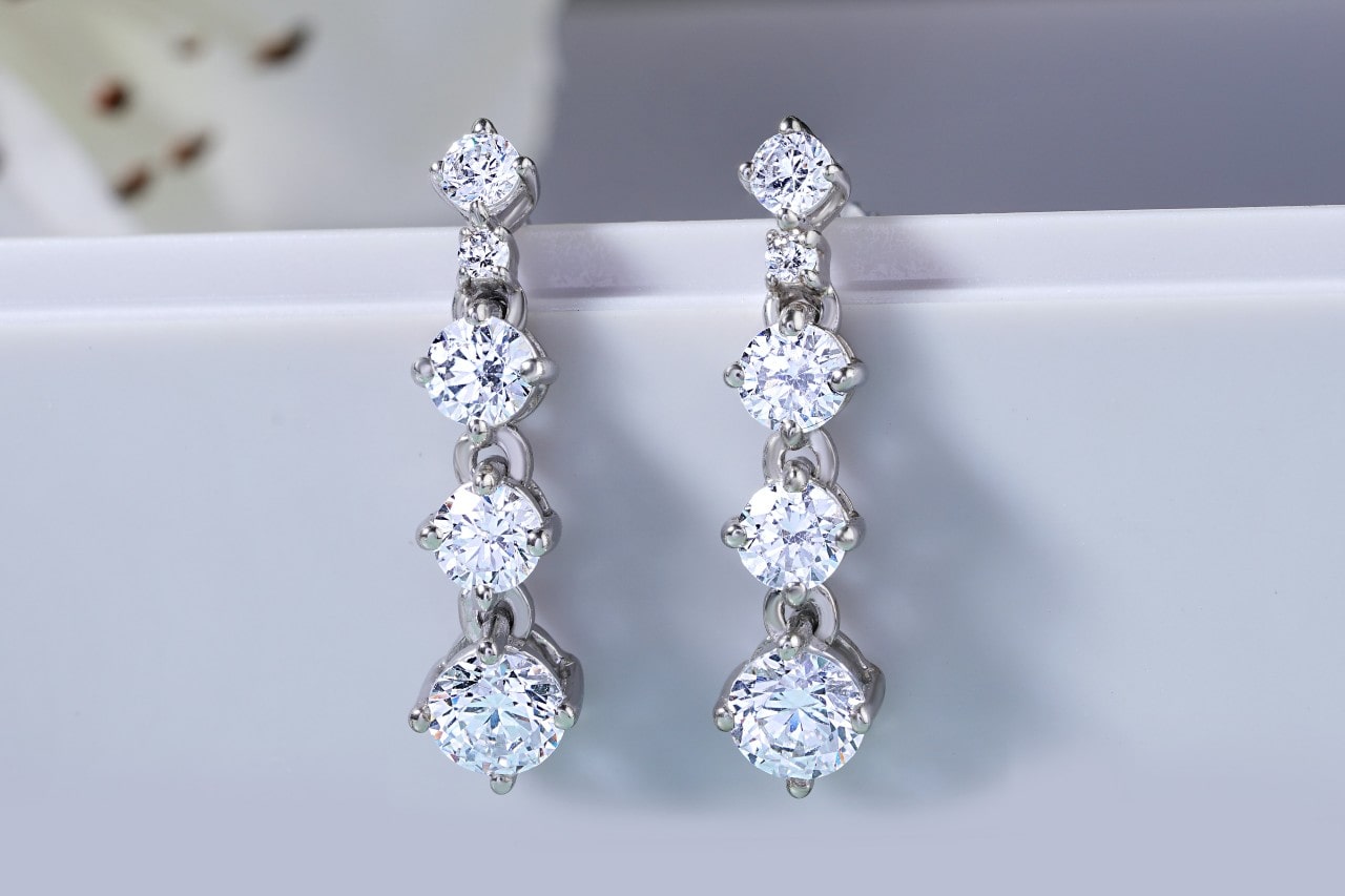 a pair of four-tiered diamond drop earrings hanging on the corner of a white surface