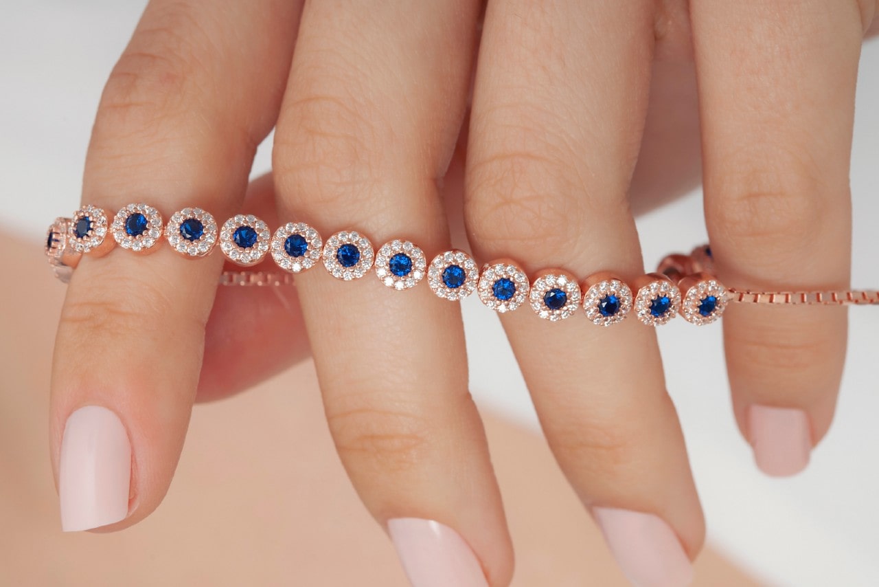 close up image of a hand holding a rose gold sapphire line bracelet, each stone surrounded by accent diamonds