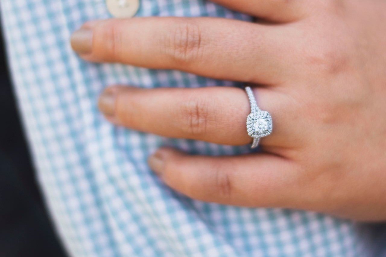 a woman with her hand on someone’s plaid sleeve, wearing a halo engagement ring