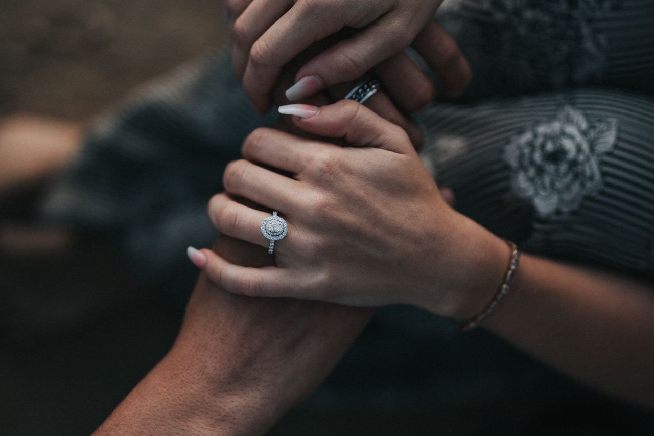 a couple holding hands, the woman wearing an oval cut halo engagement ring