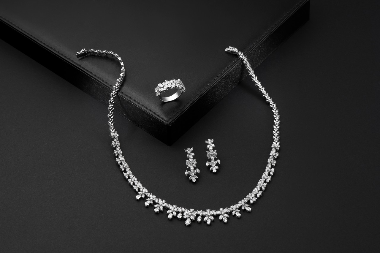 A diamond jewelry set with a sparkling necklace, matching earrings, and a ring, displayed on a black surface