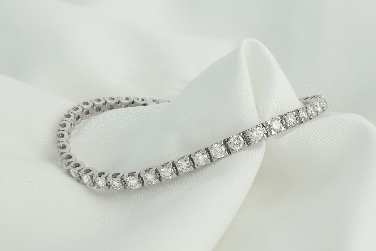 Elegant silver diamond tennis bracelet elegantly draped over soft white fabric.