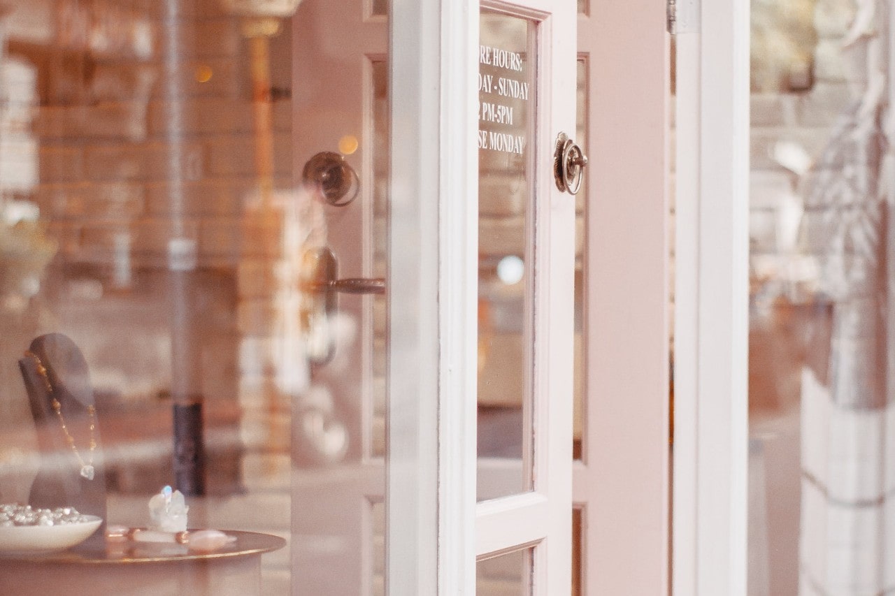 A soft pink boutique door slightly ajar, revealing a cozy interior with jewelry on display.