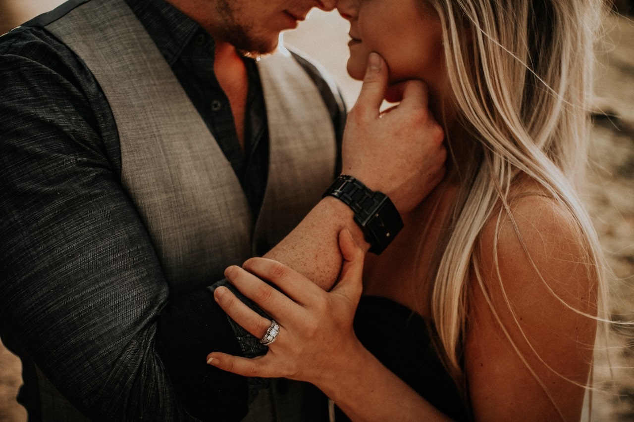 a couple intimately embraces, the woman sporting her engagement ring.