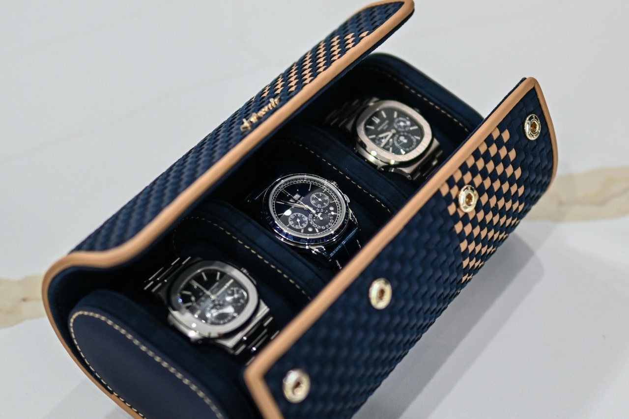 Luxurious navy and tan checkered case showcasing three elegant watches with black dials and silver bands. Luxurious navy and tan checkered case showcasing three elegant watches with black dials and silver bands.