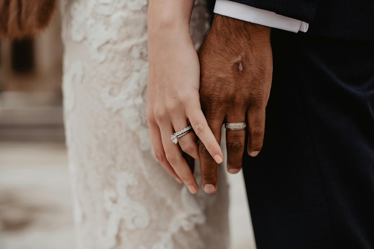 A close-up of a bride and groom holding hands, showcasing their wedding rings against the bride’s lace dress and the groom’s dark suit.